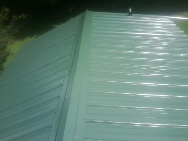 New green metal panels meeting at the ridge of a roof — Flat Roof Repair work by our crew in Tolleson