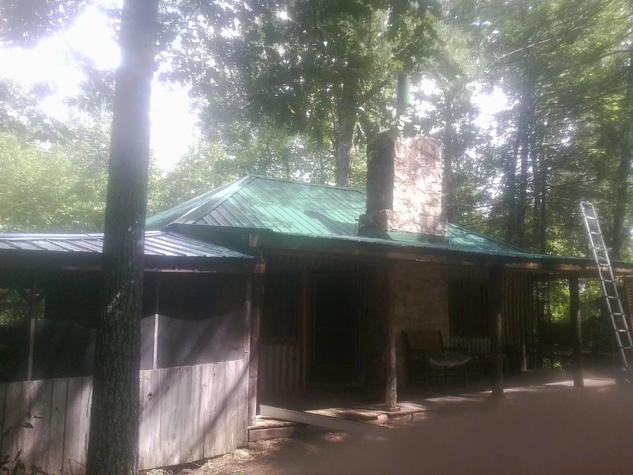 Green metal roof and stone chimney above a log cabin porch in Tolleson