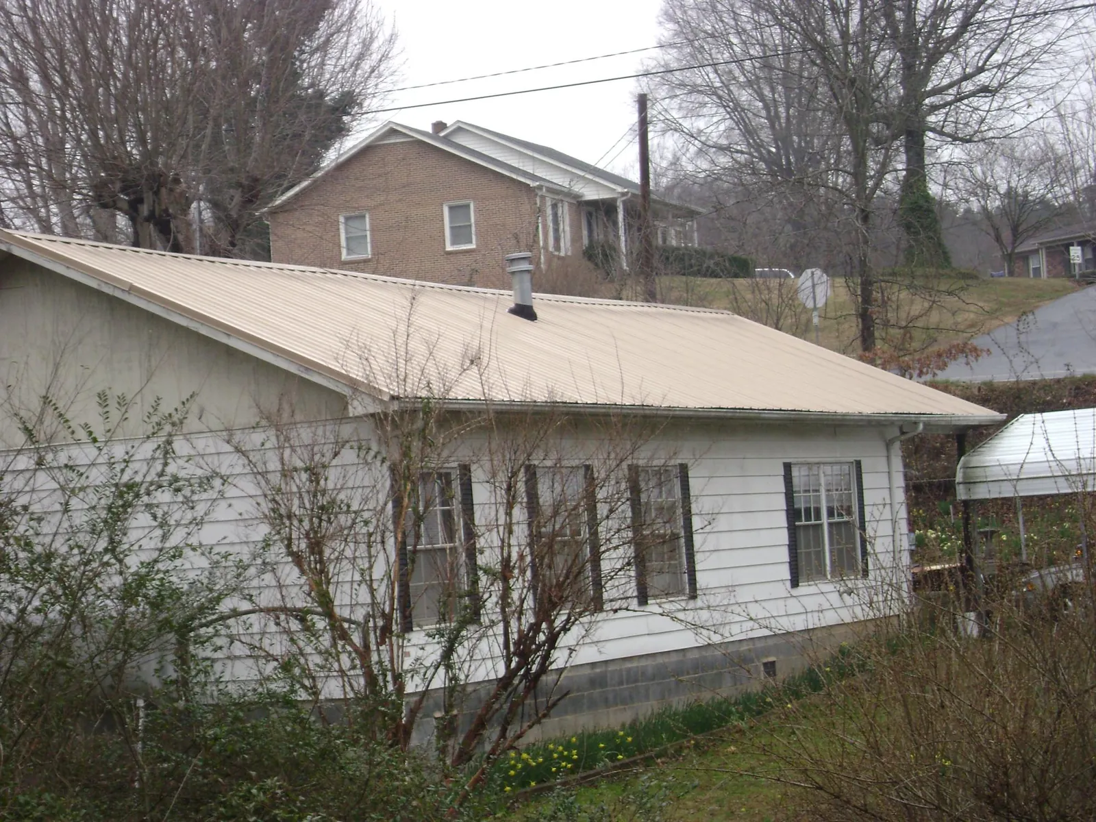 Tan metal roof on a white sided house set into a hillside — Commercial Roofing by Roofing Brothers in Tolleson